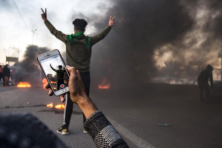 A protester uses his cell phone to film at a demonstration in Basra in January. Militias and Iraqi security forces are attacking and detaining journalists who cover protests in the city. (AFP/Hussein Faleh)