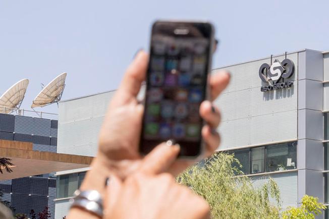 A woman uses her iPhone in front of the building housing NSO Group on August 28, 2016, in Herzliya, near Tel Aviv, Israel. The company has come under increased scrutiny for the alleged use of its spyware tool, Pegasus, to target journalists. (AFP/Jack Guez)