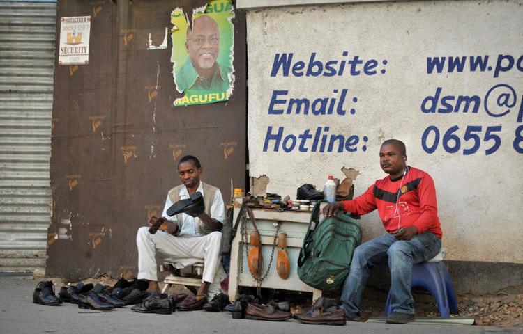A Tanzanian shoe-shiner conducts his business underneath an election poster for then ruling party presidential candidate, and later president, John Magufuli, in Dar es Salaam, Tanzania, on October 27, 2015. On March 28, 2019, the East African Court of Justice found that multiple sections of Tanzania's Media Services Act restrict press freedom. (AP Photo/Khalfan Said)