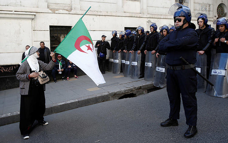 A woman carries a flag in front of police during a protest in Algiers on March 29. Amid weeks of unrest, Algerian journalists are staging their own demonstrations over censorship. (Reuters/Ramzi Boudina)