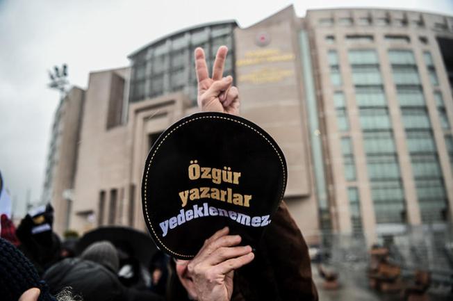 A man holds a sign reading 'Writers' freedom is not guaranteed' outside an Istanbul court during a trial connected to the now shuttered paper Özgür Gündem, in December 2016. A court sentenced seven former journalists from the paper to prison on May 21, 2019. (AFP/Ozan Kose)