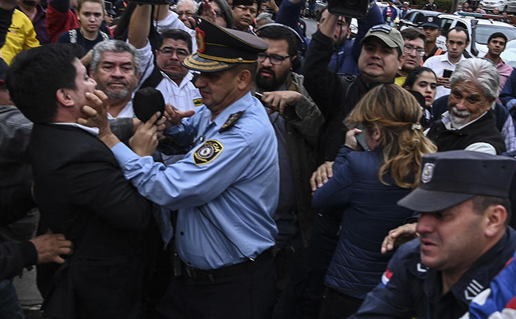 Un periodista es agarrado por un agente policial durante las protestas en Asunción, Paraguay, el 23 de julio de 2019. Por lo menos cuatro periodistas resultaron heridos durante las protestas, y una periodista fue presuntamente manoseada por un manifestante.  (AFP/Norberto Duarte)