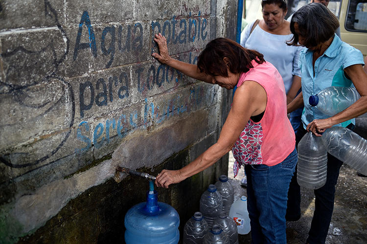 Una mujer llena un bidón de agua en una estación en San Juán de los Morros, Estado Guárico, Venezuela, el 10 de julio de 2018. El 18 de julio de 2019 un periodista fue detenido en San Juán de los Morros bajo la ‘ley del odio’ venezolana por criticar a un político regional. (AFP/Federico Parra)
