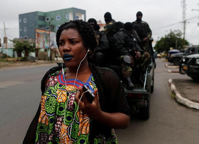 A woman walks past Rapid Intervention Battalion members as they patrol in the city of Buea in October 2018. CPJ and others are calling on the ACHPR to address human rights violations in Cameroon's Anglophone regions. (Reuters/Zohra Bensemra)