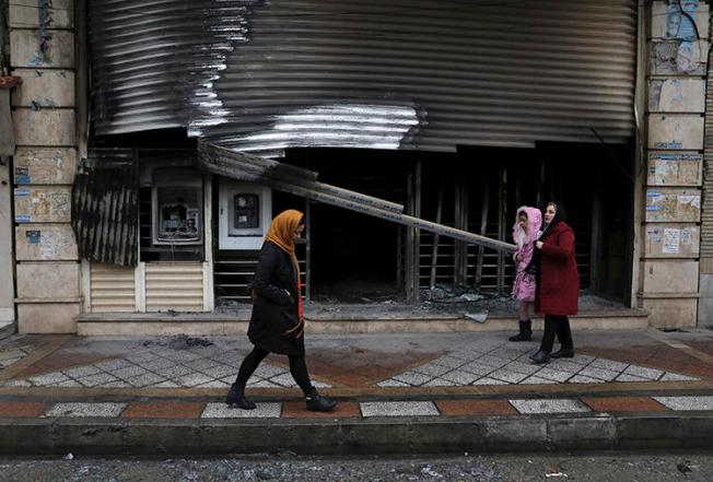 People walk past a building that was burned during recent protests in Shahriar, Iran, on November 20, 2019. Journalist Mohammad Mosaed was recently arrested after tweeting during an internet shutdown imposed amid the protests. (AP/Vahid Salemi)