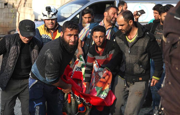 Residents and a rescue worker carry the body of a man killed in an airstrike in Kfar Rumah, in Syria's Idlib province, on November 10, 2019. A journalist for the Kafr Rumah Media Office was killed during shelling in the town. (AFP/Abdulaziz Ketaz)