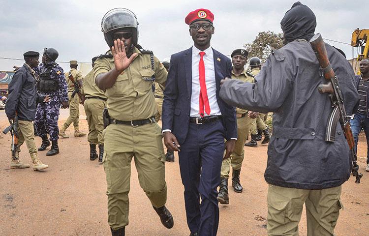 Ugandan opposition politician and popular musician Robert Kyagulanyi, also known as Bobi Wine (C), is escorted by a police officer as he is arrested on charges of unlawful assembly before starting his first public meeting ahead of presidential election next year, on January 6, 2020, in Kasangati town, a suburb of Kampala. Ugandan journalist Moses Bwayo was charged with illegal assembly and held in prison on March 4. (AFP/Stringer)