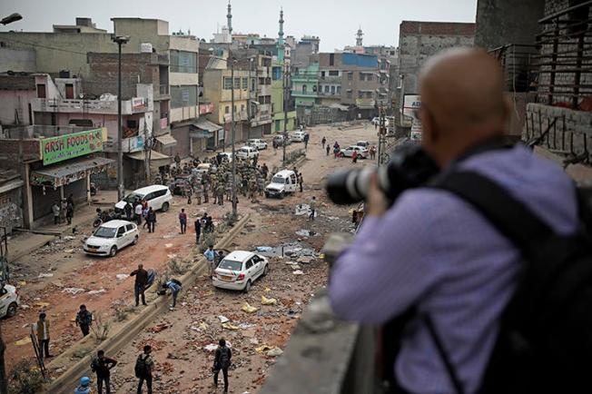 A journalist photographs soldiers patrolling a street following riots in New Delhi, India, on February 27, 2020. At least a dozen journalists were attacked or harassed covering the riots. (AP/Altaf Qadri)