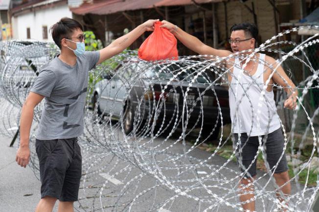 A man collects supplies over barbed wire in the coronavirus lockdown area of Selayang Baru, outside of Kuala Lumpur, Malaysia, on April 26, 2020. A journalist faces prison time over her social media posts on the health crisis. (AP/Vincent Thian)
