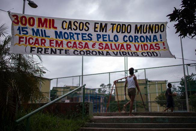 A banner reading “300,000 cases in the world, 15,000 deaths because of coronavirus! Stay at home and save lives!” hangs at the Cidade de Deus favela in Rio de Janeiro, Brazil, on April 7, 2020, during the COVID-19 outbreak. Rio’s community journalists face daily challenges informing favela residents about COVID-19. (AFP/Mauro Pimentel)