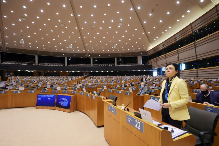 A woman in a yellow jacket stands at a row of work benches in the European Parliament.