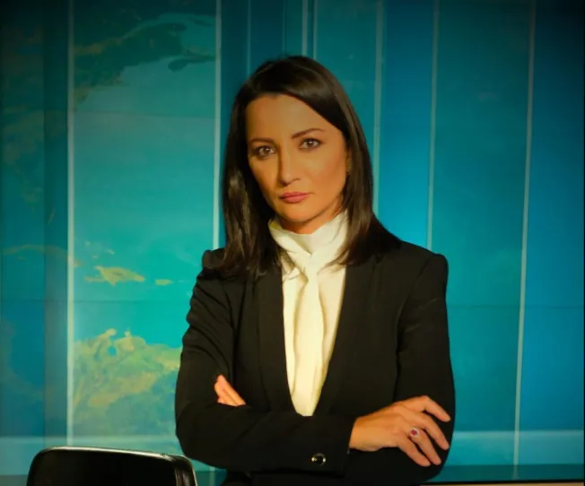 Portrait of Ghada Oueiss facing camera with arms folded in a newsroom
