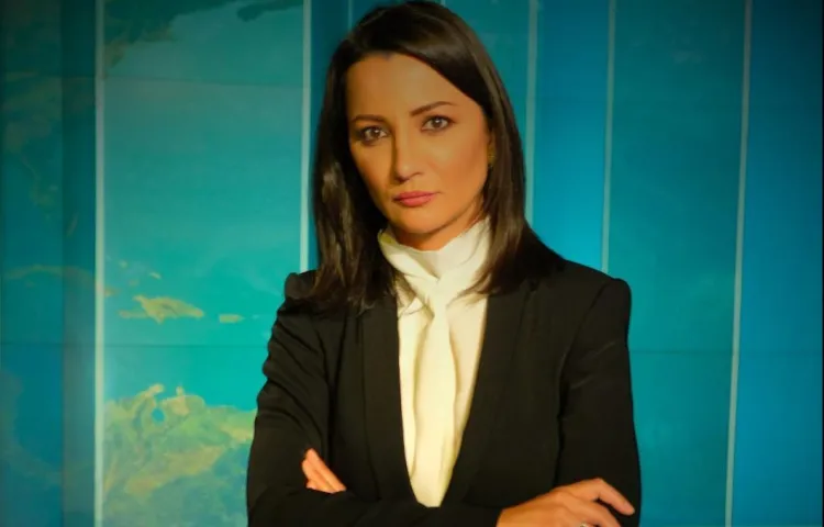 Portrait of Ghada Oueiss facing camera with arms folded in a newsroom