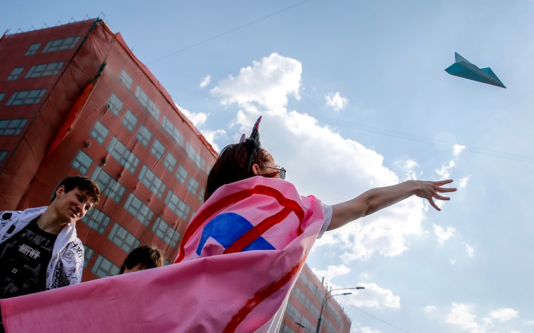 A woman throws a paper plane into the blue sky.
