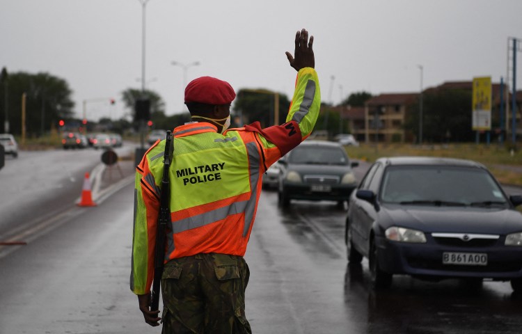 An armed officer on a street raises his hand to stop cars.