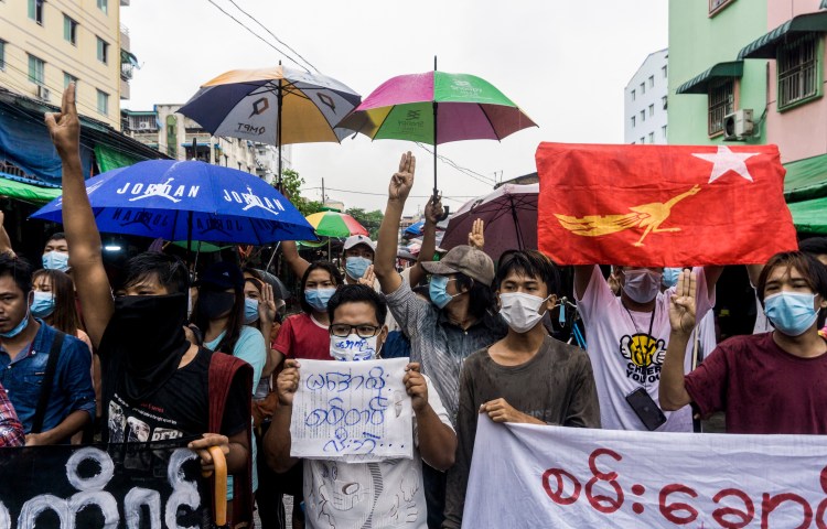 A group of people holding protest signs and umbrellas gather in a city street.