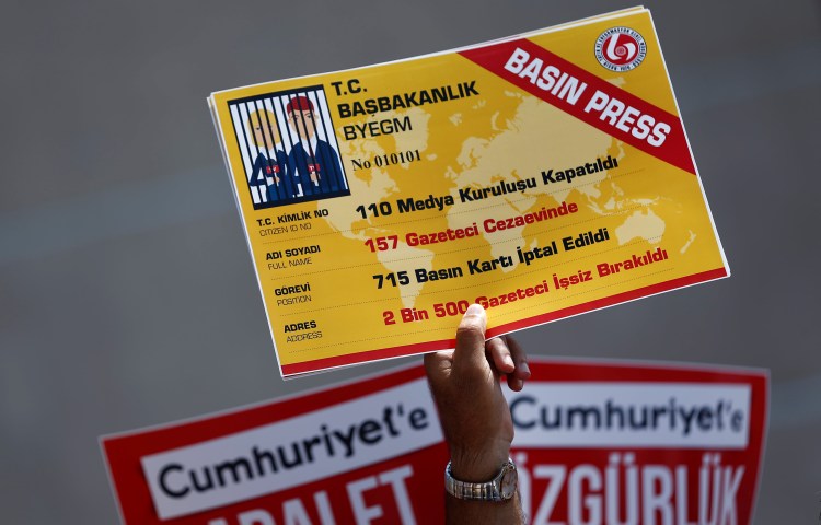 A raised hand holds a large ID card showing journalists in jail in place of a photo.