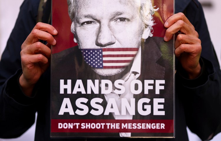 Someone holds a sign that reads "Hands off Assange: Don't shoot the messenger"