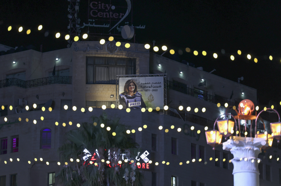 An illuminated poster of slain Palestinian-American journalist Shireen Abu Akleh hangs on a building overlooking a decorated market street as Palestinians shop in the city of Ramallah in the West Bank, on the eve of the Muslim Eid al-Adha holiday on July 8, 2022. (Photo by ABBAS MOMANI / AFP)