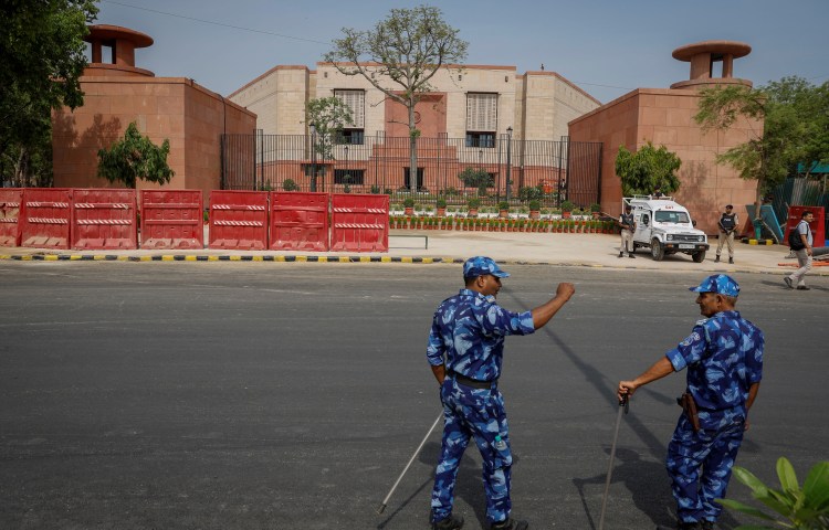 Two policemen in blue uniforms stand in front of India's parliament building in New Delhi.
