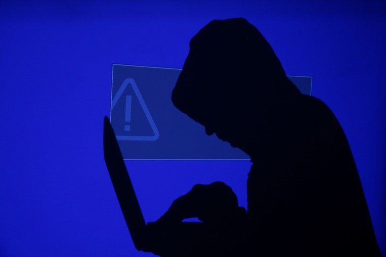 A hooded man holds a laptop as blue screen with an exclamation mark is projected on him in this illustration picture taken on May 13, 2017. (Reuters/Kacper Pempel)