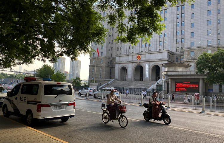 People ride past a police van outside the No. 2 Intermediate People's Court ahead of Australian writer Yang Hengjun's espionage trial in Beijing, May 27, 2021. (Photo: AP/Andy Wong)