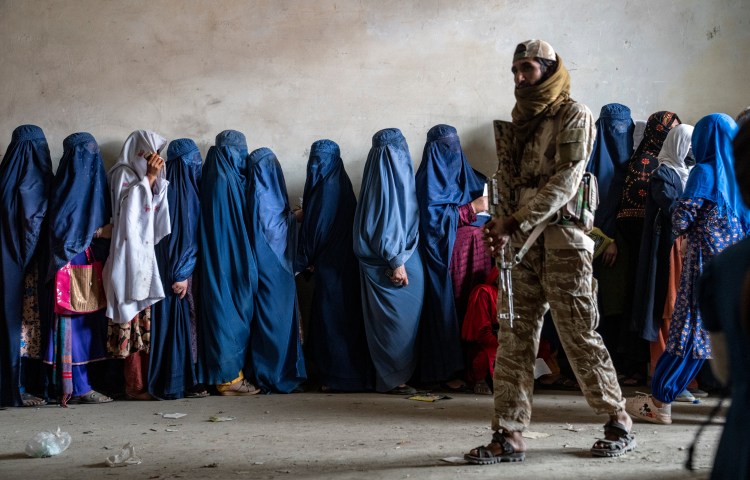 A Taliban fighter stands guard as women wait for humanitarian aid in Kabul, Afghanistan, in May 2023.