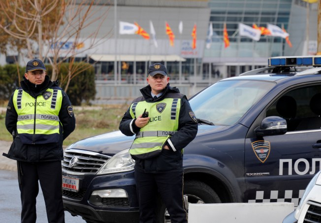 Two police officers stand in front of a police car.