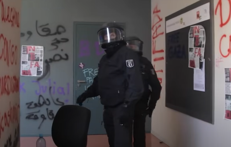 Two police officers stare down a hall with grafetti-covered walls.