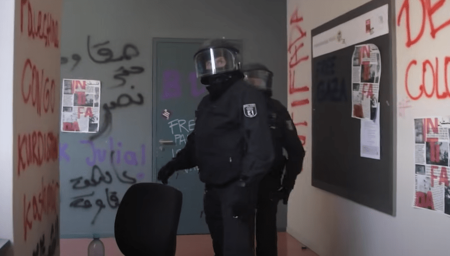 Two police officers stare down a hall with grafetti-covered walls.