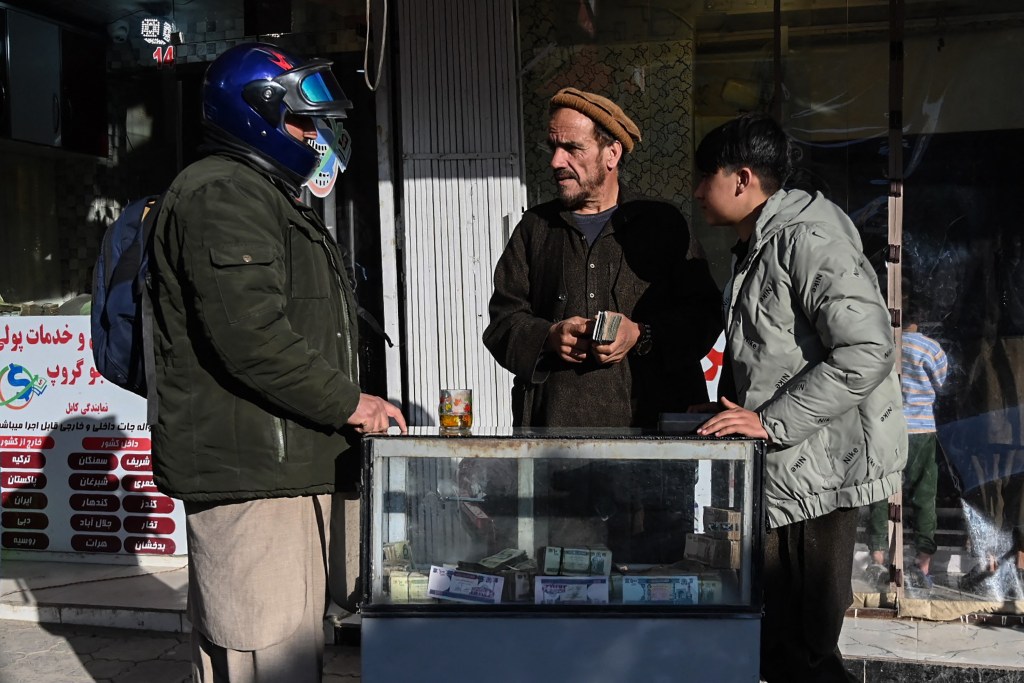 An Afghan money changer holding banknotes speaks with a customer at a currency exchange market in Kabul in January, following the decline in the afghani currency against US dollars.