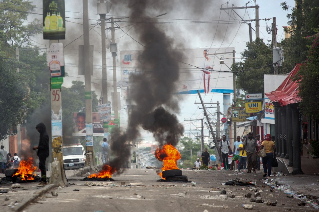 People walk past a burning barricade during a protest against insecurity, in Port-au-Prince, Haiti, April 16, 2025. REUTERS/Fildor Pq Egeder