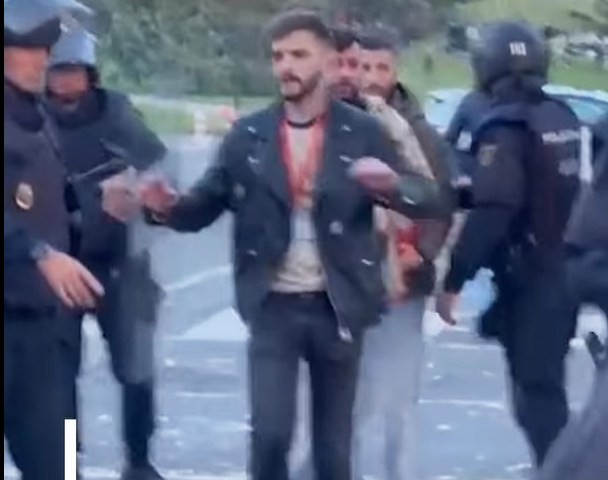 After a violent assault by masked protesters, journalist José Ismael Martínez reaches riot police for protection during clashes in Pamplona on October 30, 2025.