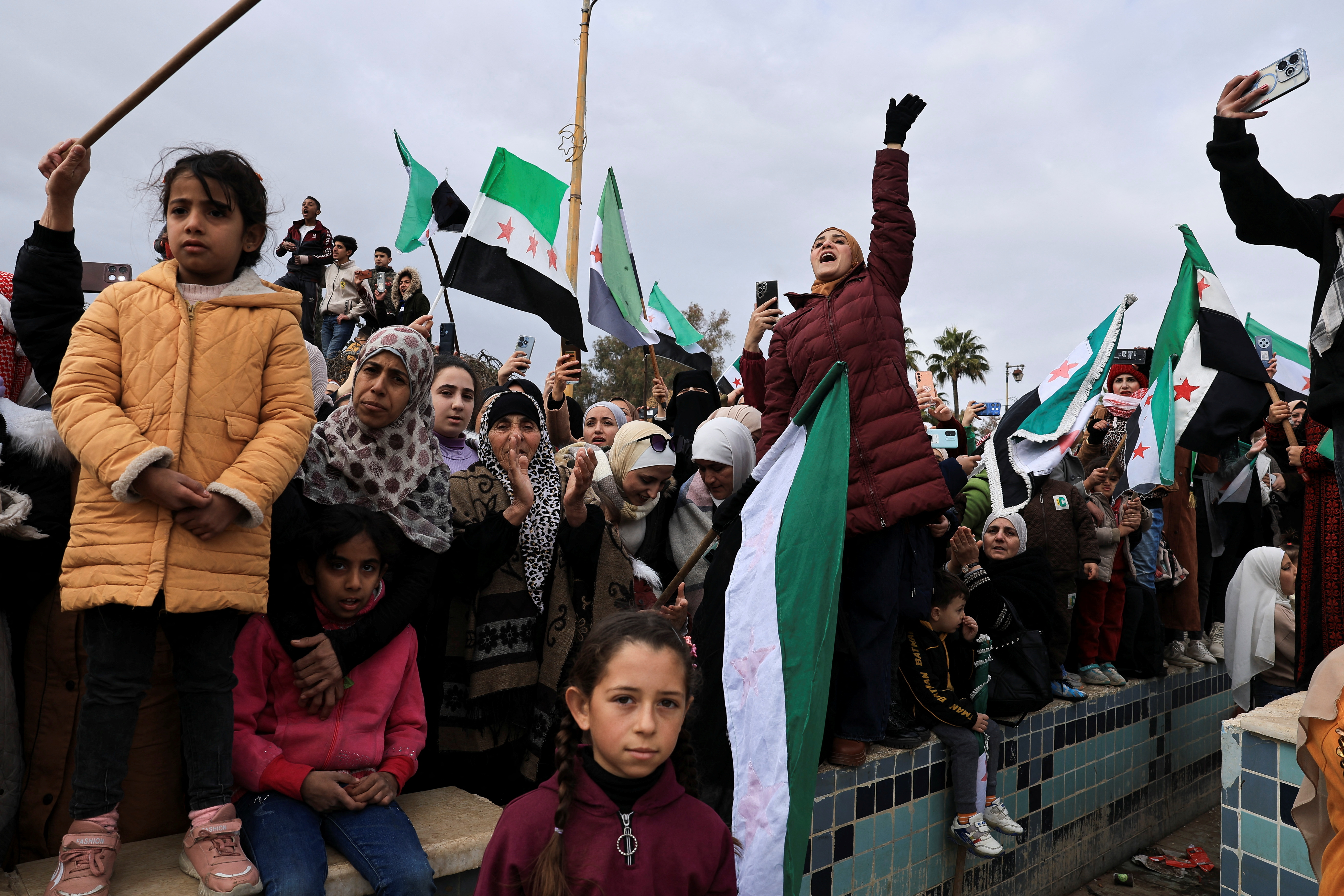People hold flags adopted by the new Syrian rulers, to celebrate after the ousting of President Bashar al-Assad in Daraa in December 2024.