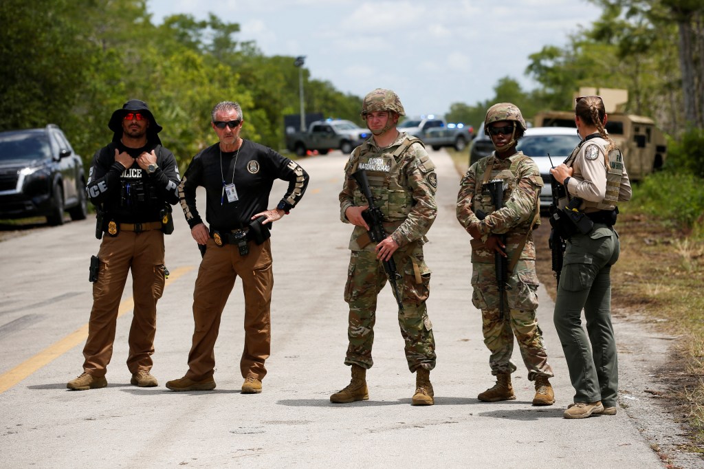 Members of the Florida National Guard and law enforcement officers monitor a protest at an entrance road of a temporary migrant detention center nicknamed "Alligator Alcatraz" on the day of a visit by U.S. President Donald Trump in Ochopee, Florida, U.S., July 1, 2025. REUTERS/Octavio Jones