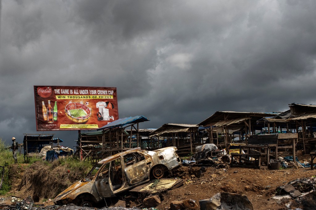 The wreckage of burnt out car, allegedly destroyed by separatist fighters, as a Cameroonian soldier (left) patrols the edge of the abandoned market in the majority Anglophone South-West region in Buea, in 2018.