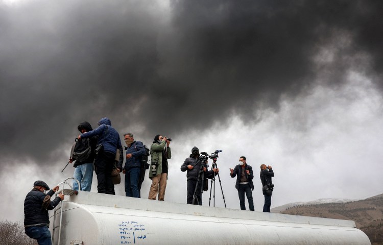 Journalists stand atop a fuel tanker as they cover a nearby fire following an overnight airstrike on the Shahran oil refinery in northwestern Tehran on March 8, 2026.