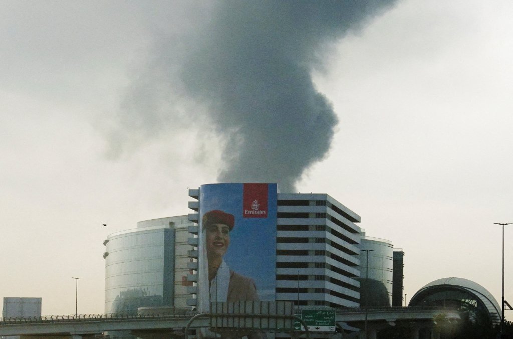 Smoke rising from an area near the Dubai International Airport is seen through the windshield of a vehicle, after a drone attack hit a fuel tank, according to Dubai authorities, on March 16, 2026.