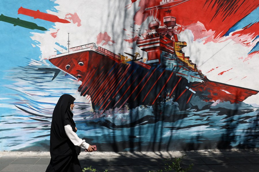 A woman walks next to a mural on a street in Tehran, Iran, May 18, 2026.